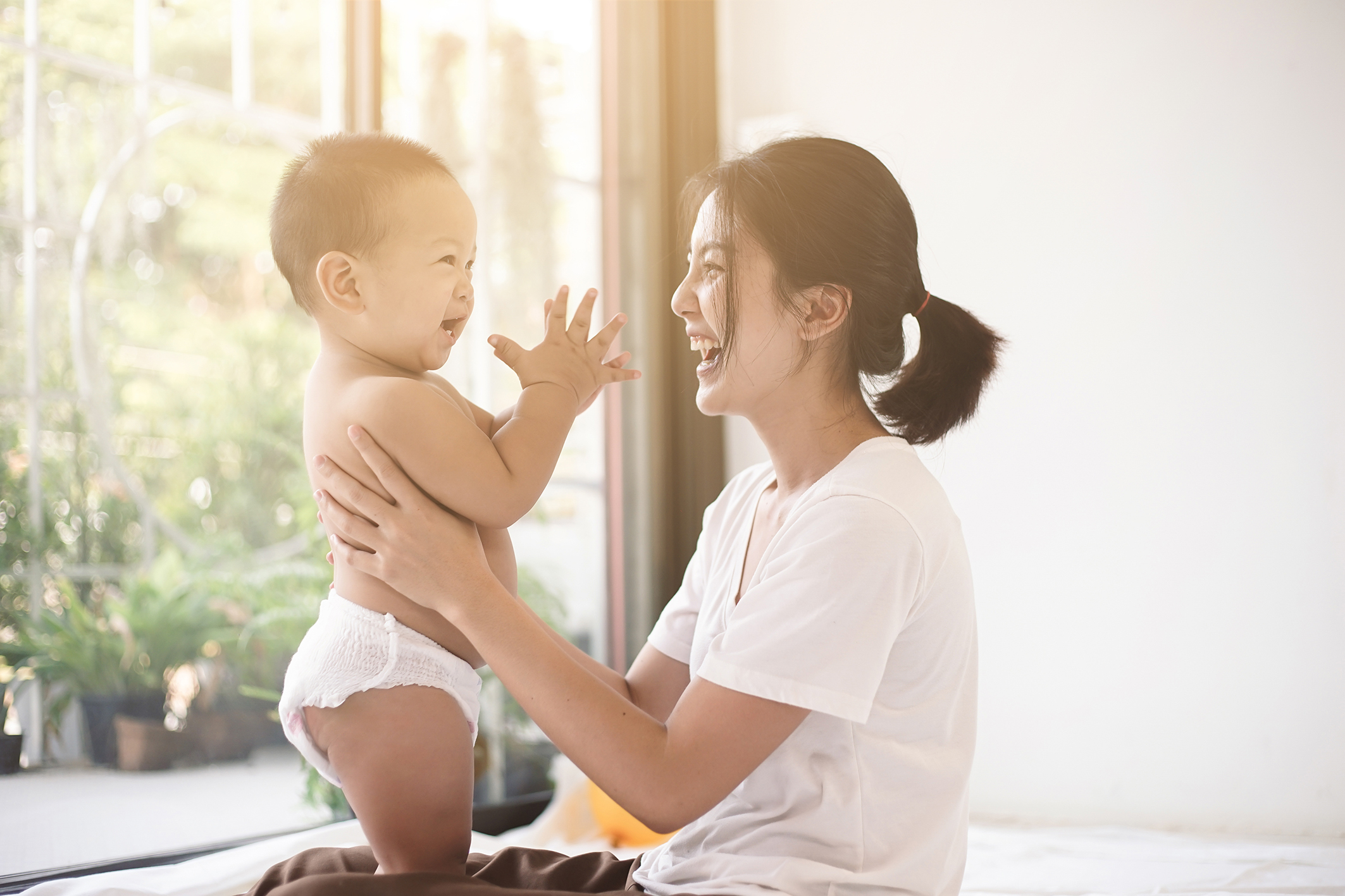 Image of smiling mother holding baby who is clapping hands and smiling