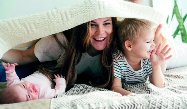Happy Mommy Plays With The Children On The Bed And Covers