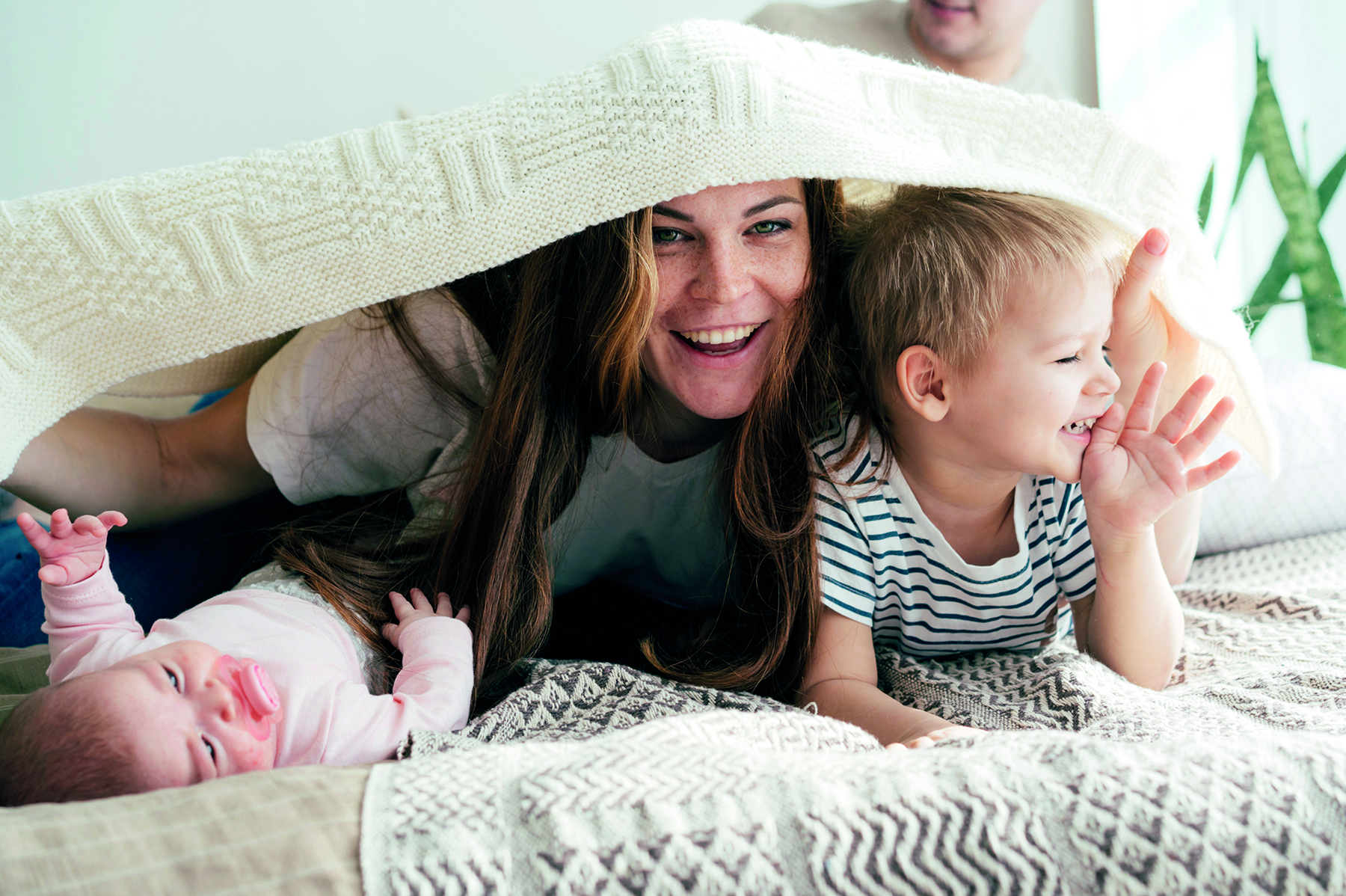 Happy Mommy Plays With The Children On The Bed And Covers