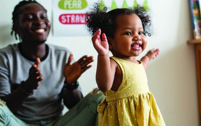 Image of smiling toddler playing while her mother watches and claps